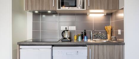 A compact kitchen with a built-in microwave, a kettle, and a dishwasher.