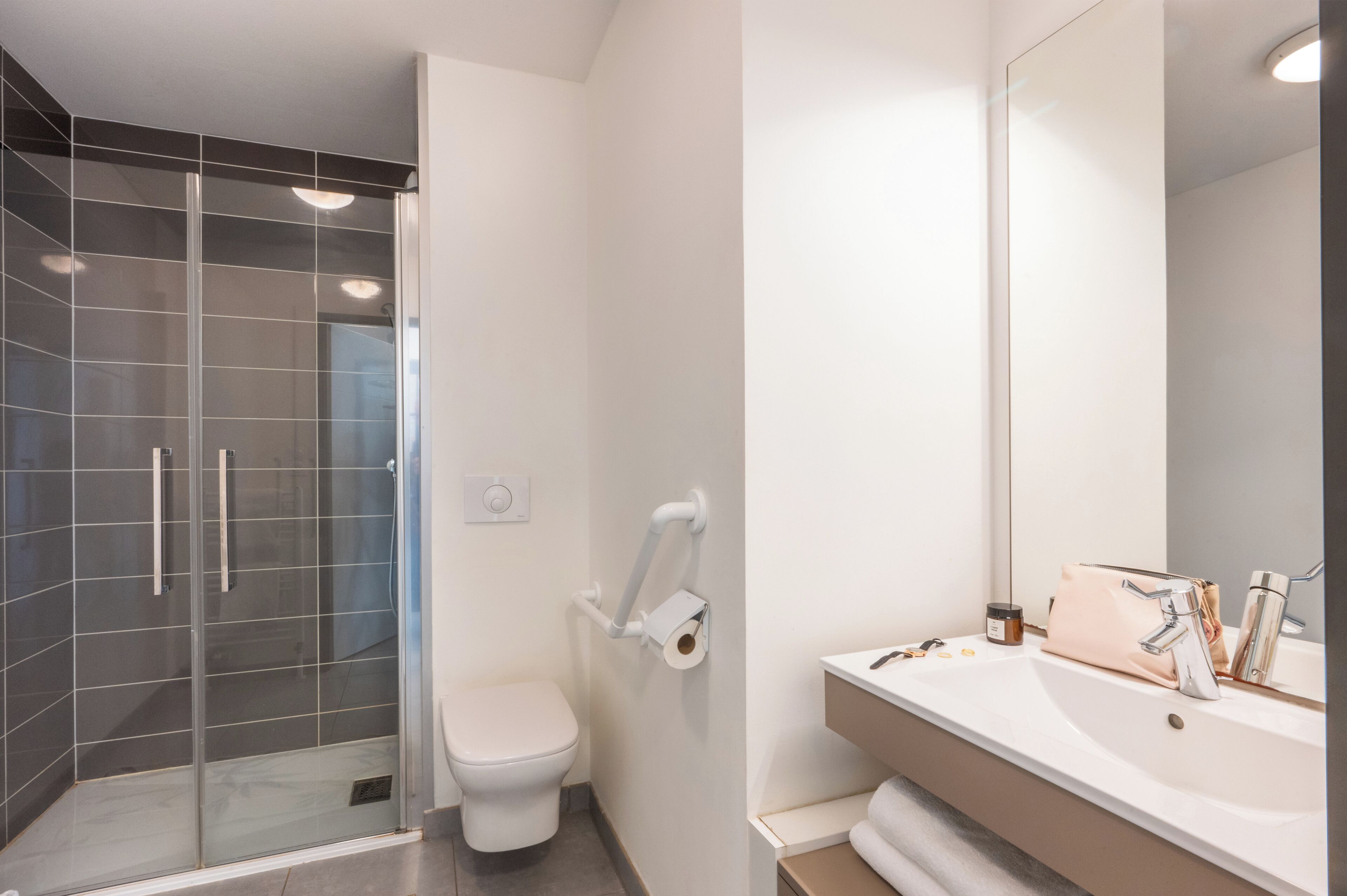 A modern bathroom with a glass shower enclosure, a toilet, and a sink with a mirror.