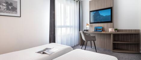 Habitación de hotel con dos camas, un escritorio con computadora, un televisor y un cuadro en la pared.