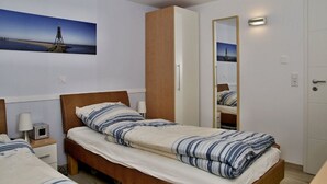 Ein Schlafzimmer mit zwei Betten, einem Kleiderschrank, einem Spiegel und einem Gemälde eines Leuchtturms.