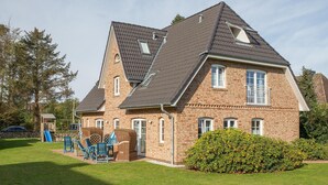 A two-story house with a sloped roof, brick exterior, and a small garden area with a hedge. - Holiday home in Süddorf on the island Amrum, island, national park, close to the (Süddorf)