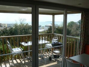 A balcony with a table and chairs, a grill, and a view of the sea and buildings. - Camping Les Sables Blancs (Concarneau)