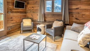 A cozy log cabin interior with a sofa, armchairs, a coffee table, and a TV mounted on the wall. - Cozy Chalet - 1 BR - 4 Pers - Terrace - Parking (La Clusaz)