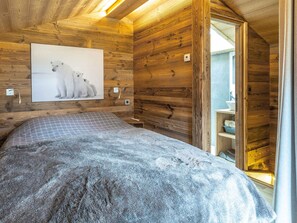 A cozy wooden cabin room with a bed, a painting of polar bears, and a wooden shelf with a bowl.