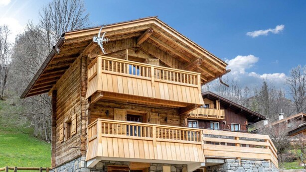 A multi-story wooden chalet with balconies, stone foundation, and a wooden deck. - Cozy Chalet - 1 BR - 4 Pers - Terrace - Parking (La Clusaz)