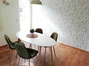 Un coin repas avec une table blanche, quatre chaises, une petite plante en pot et un mur orné d’un motif floral.