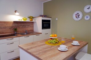 Una cocina moderna con armarios blancos, encimera de madera, horno empotrado y una pequeña zona de comedor con frutas y tazas de café.