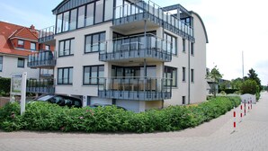 A modern multi-story residential building with balconies, a paved driveway, and a well-maintained garden. - Beachhouse (Cuxhaven)