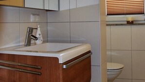 A bathroom with a wooden vanity, a white sink, and a toilet. - Beachhouse (Cuxhaven)