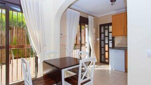 Un comedor con mesa y sillas, una cocina al fondo y un balcón con cortinas.
