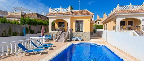 A swimming pool with lounge chairs, a staircase, and a building with a tiled roof.