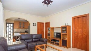 Una sala de estar con sofá, mesa de centro, mueble para televisión y armarios de madera.