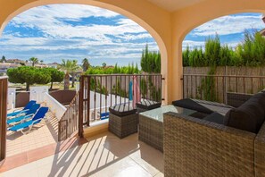 A balcony with wicker furniture, a view of the neighborhood, and a clear sky.