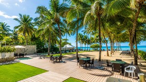 A resort with a pool, outdoor seating, palm trees, and a view of the ocean. - Beachfront | Ocean View Balcony | Pool & Jacuzzi (Playa Juan Dolio)