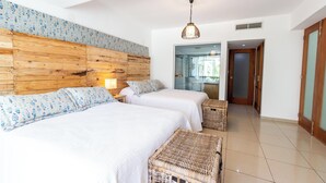 A hotel room with two beds, a wooden headboard, a wicker bench, and a large window. - Beachfront | Ocean View Balcony | Pool & Jacuzzi (Playa Juan Dolio)
