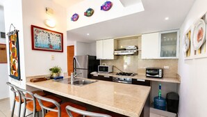 A modern kitchen with a central island, bar stools, a refrigerator, microwave, oven, and a sink. - Beachfront | Ocean View Balcony | Pool & Jacuzzi (Playa Juan Dolio)