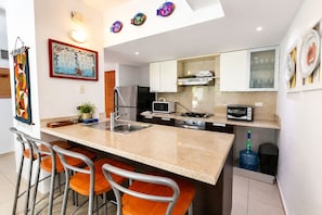 Una cucina moderna con isola centrale, sgabelli da bar, microonde, piano cottura e frigorifero.