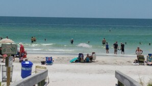 Una spiaggia con persone che nuotano e prendono il sole, una torretta di salvataggio e sedie a sdraio.