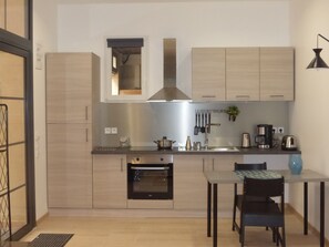 A compact kitchen with a built-in oven, a coffee maker, and a dining area with a table and chairs.