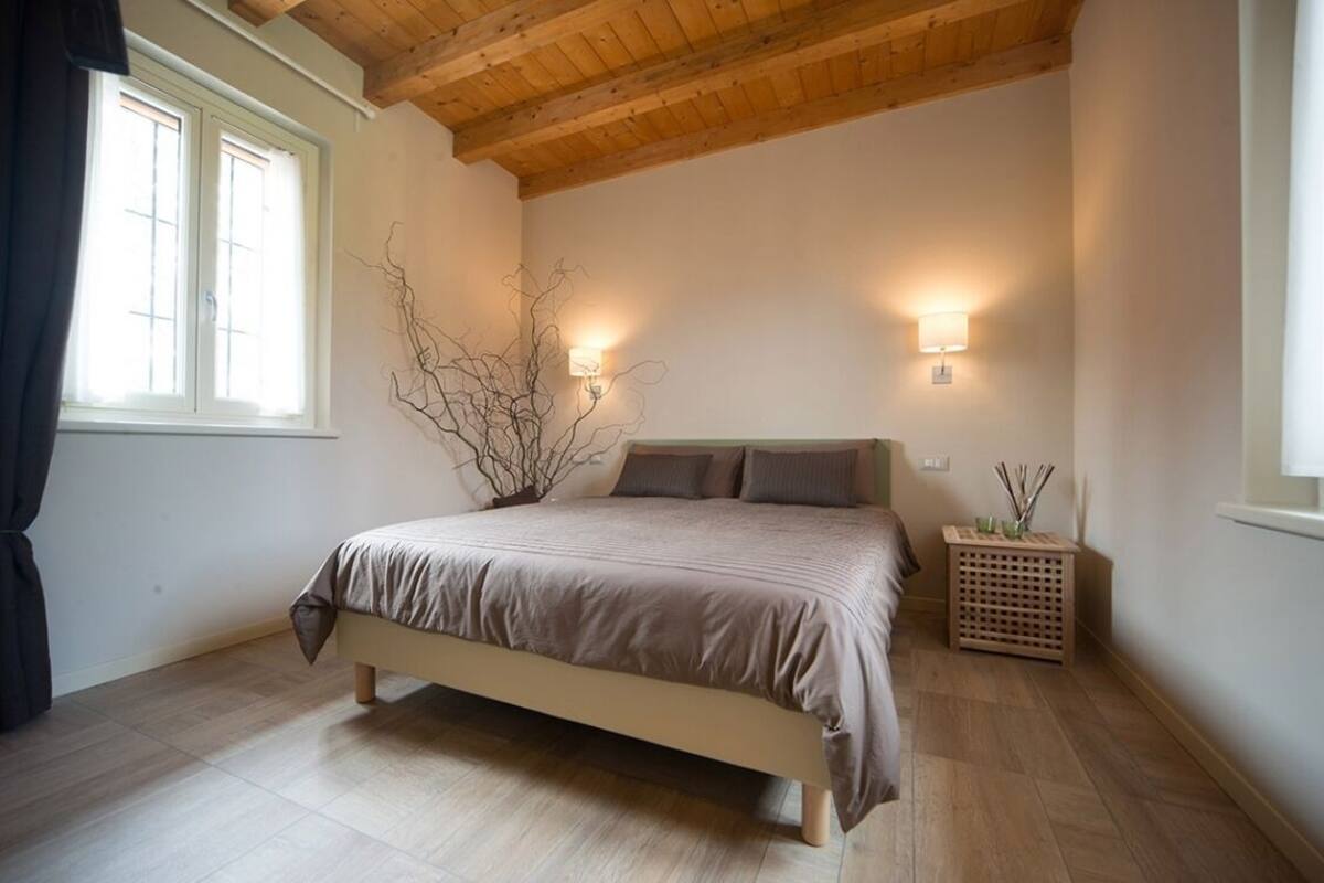 A bedroom with a bed, two wall-mounted lights, a window with curtains, and a wooden floor.
