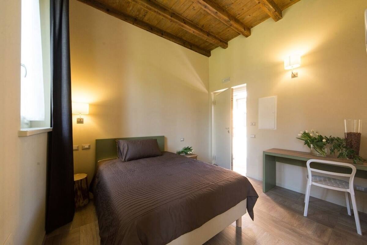 A bedroom with a bed, bedside table, lamp, and a desk with a chair.