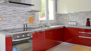 Una cocina moderna con una decoración en tonos rojo y blanco, que incluye un lavamanos de acero inoxidable, un horno empotrado y un ventanal que proporciona luz natural.