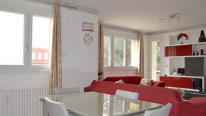 Una habitación con una mesa de vidrio, sillas blancas, un sofá rojo y una estantería con repisas rojas y blancas.