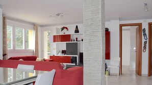 Una sala de estar moderna con un sofá rojo, una mesa de comedor de vidrio y una zona de cocina con armarios rojos.