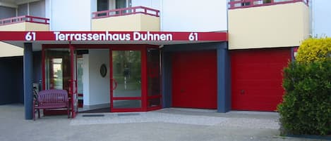 A building with a red and white facade, numbered 61, with a red door and a bench outside.