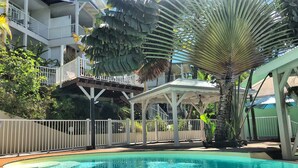 A pool area with a clear blue pool, a covered seating area, and a white fence.