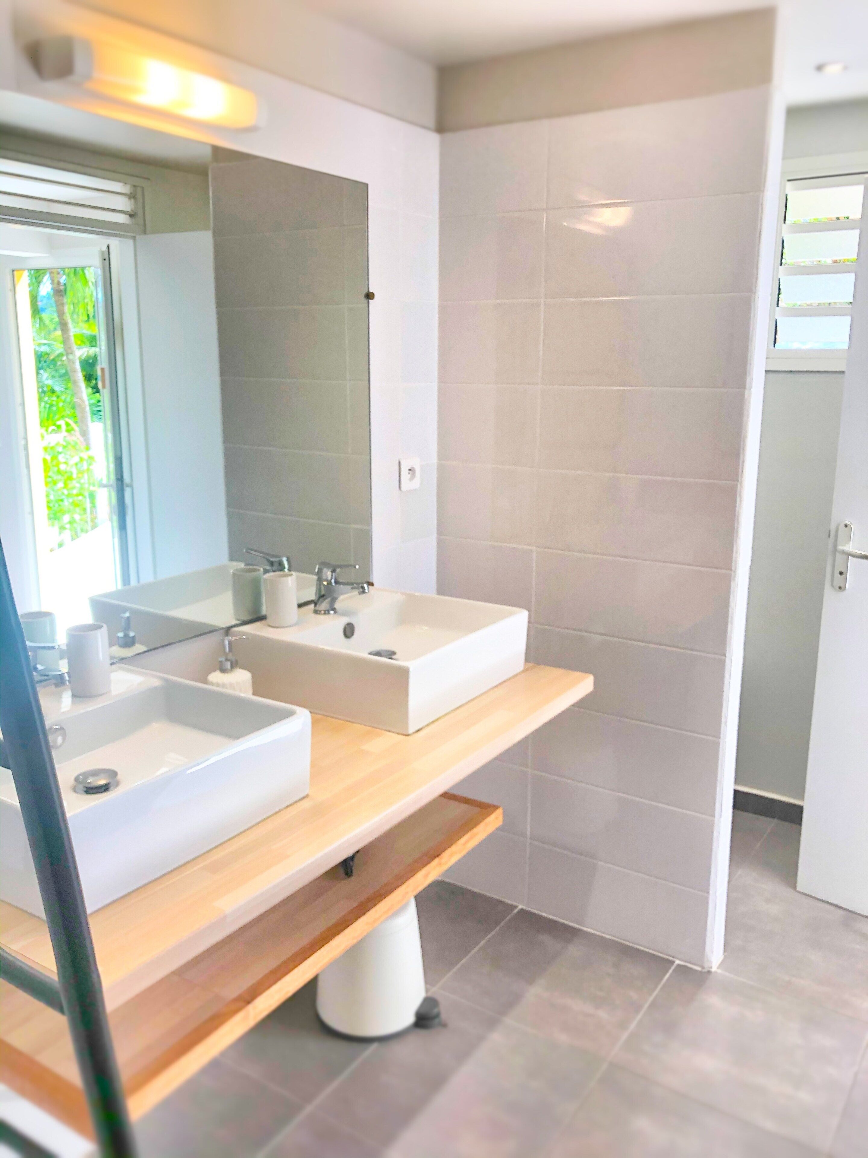 Une salle de bain moderne avec deux lavabos, un miroir et un espace douche.