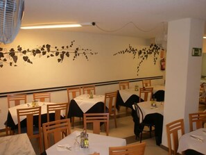 A restaurant interior with multiple tables and chairs, a decorative wall with a vine design, and a fire extinguisher mounted on the wall. - Mayna (Benidorm)