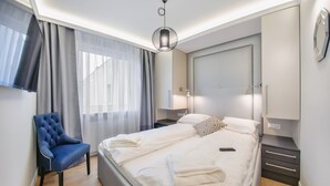 A modern hotel room with a neatly made bed, a blue armchair, and a large mirror on the wall. - Apartamenty Sun & Snow Centrum - Plaża (Sopot)