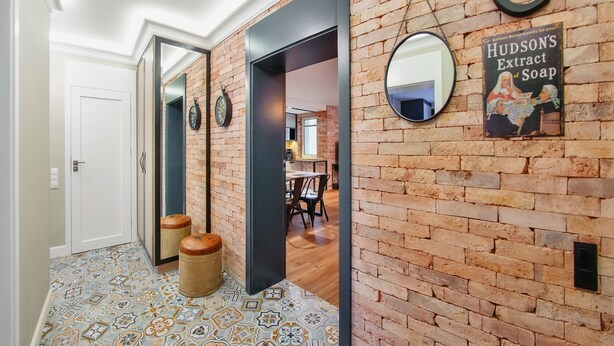 A hallway with a brick wall, a mirror, a poster, and a patterned floor. - Apartamenty Sun & Snow Centrum - Plaża (Sopot)