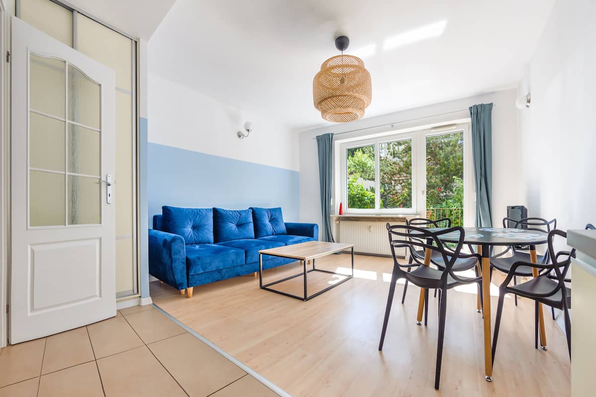 Een moderne woonkamer met een blauwe bank, een houten salontafel en een eethoek met een ronde tafel en stoelen.
