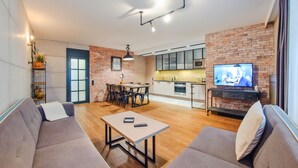 A modern living room with a sofa, a coffee table, and a TV. There is a kitchen area with a microwave and cabinets. - Apartamenty Sun & Snow Centrum - Plaża (Sopot)