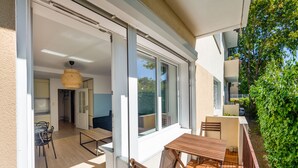 An open-plan living area with a dining table and chairs, a kitchen area, and a sliding glass door leading to a balcony with a wooden table and chairs. - Apartamenty Sun & Snow Centrum - Plaża (Sopot)