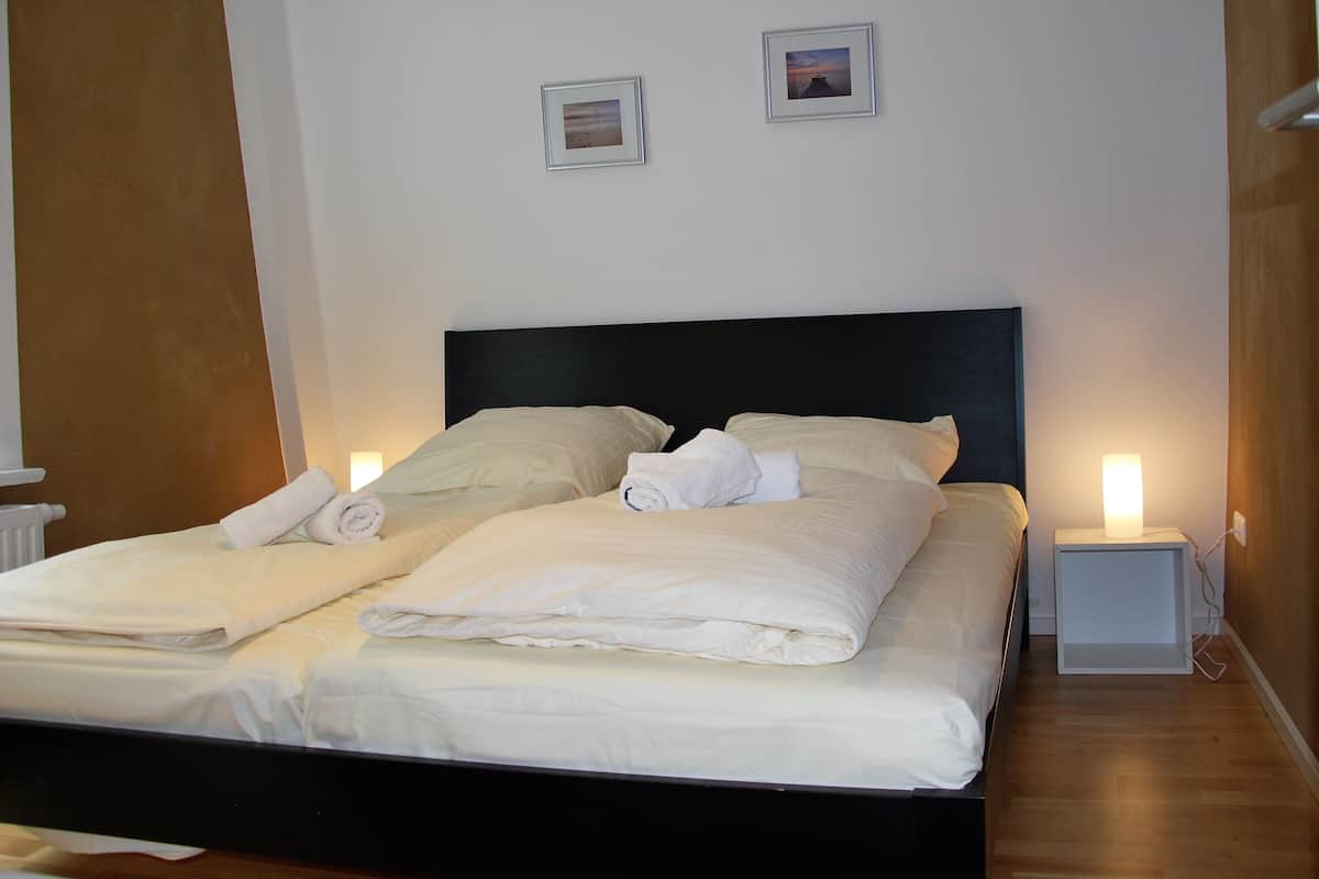 Un lit bien fait, avec du linge de lit blanc et une tête de lit noire, dans une chambre d’hôtel.