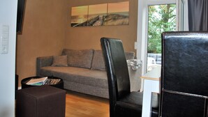 A living room with a sofa, a black leather chair, a coffee table, and a painting on the wall.