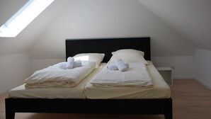 A twin bed with white linens and towels, a black headboard, and a skylight in a simple, clean room.