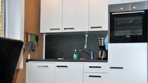 A compact kitchen with white cabinets, a black countertop, a coffee maker, and a Siemens oven.