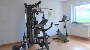 Une salle de sport équipée d’une machine de musculation, d’un vélo elliptique et d’un banc.