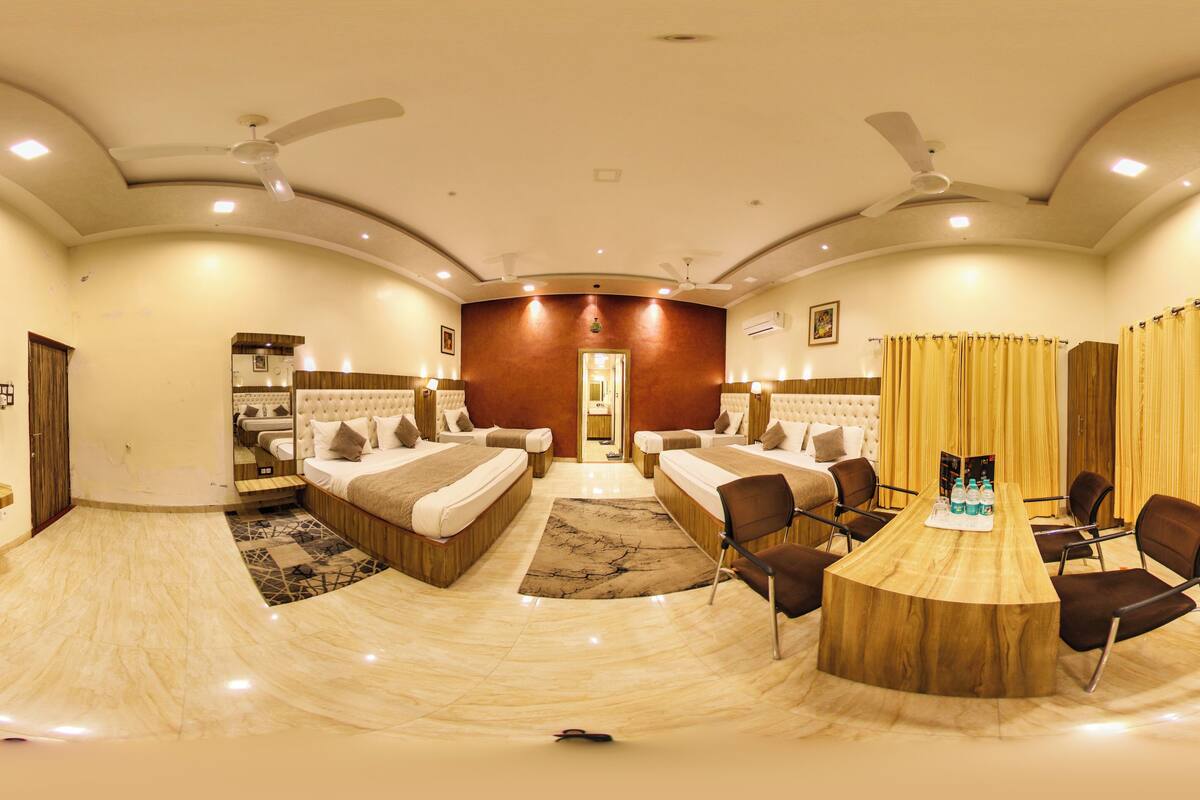 A spacious hotel room with a large bed, a TV, a seating area, and a dining table.