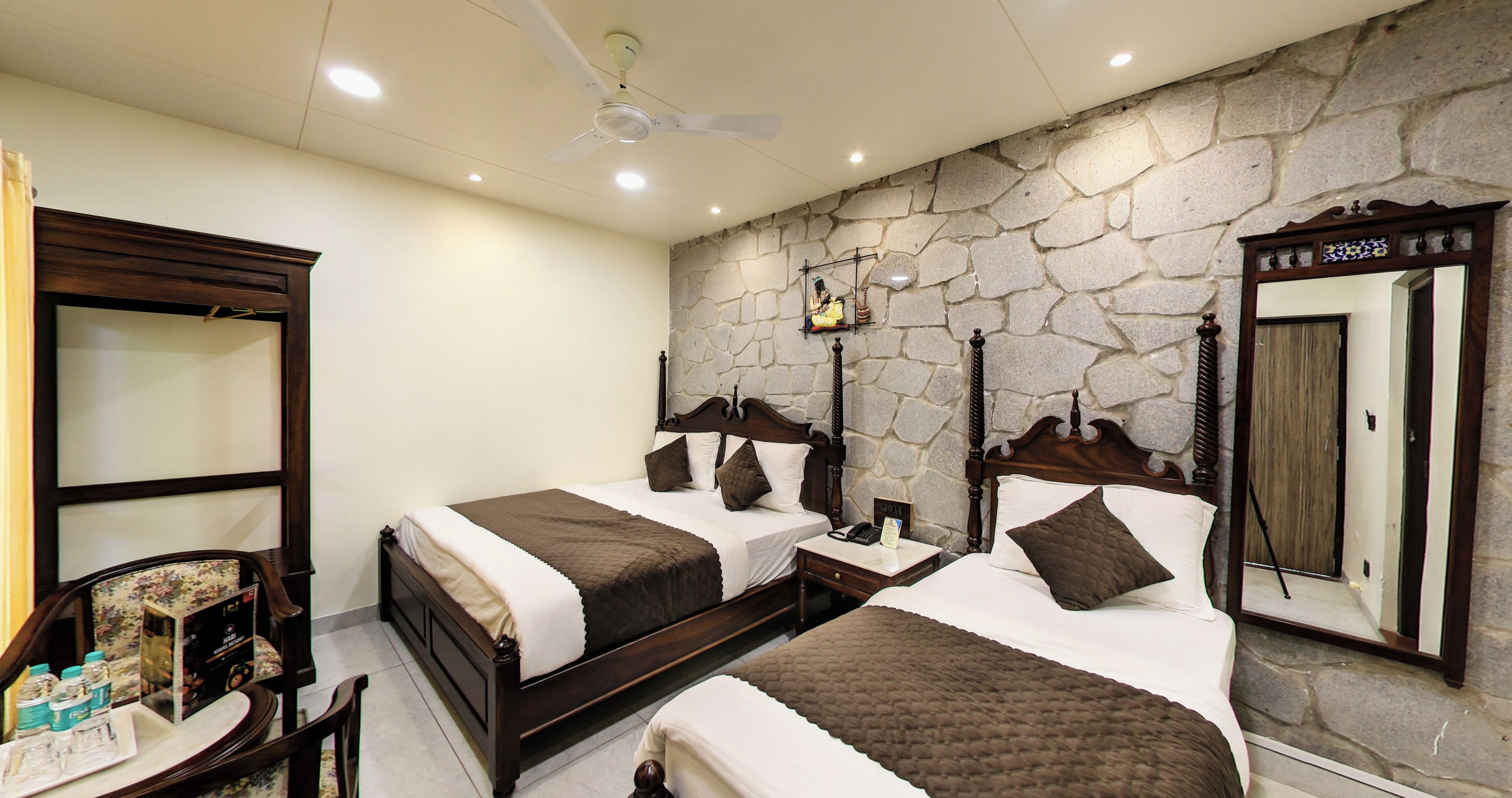 A hotel room with two beds, a stone wall, a ceiling fan, and a large mirror.