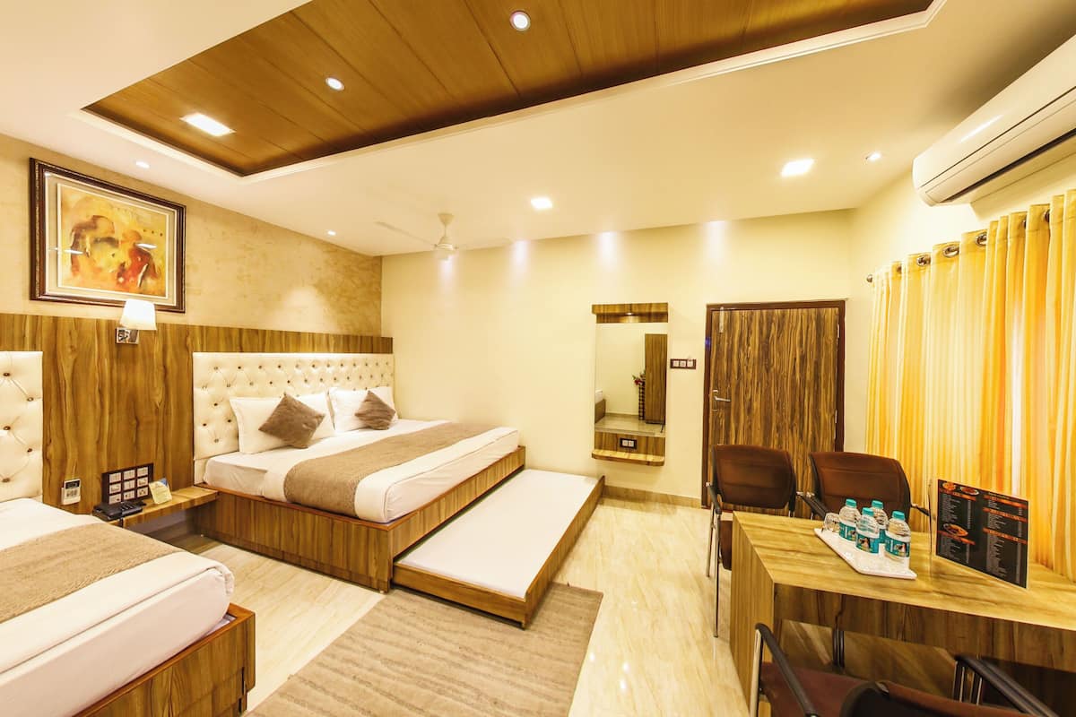 A hotel room with a bed, a desk, chairs, and an air conditioning unit.