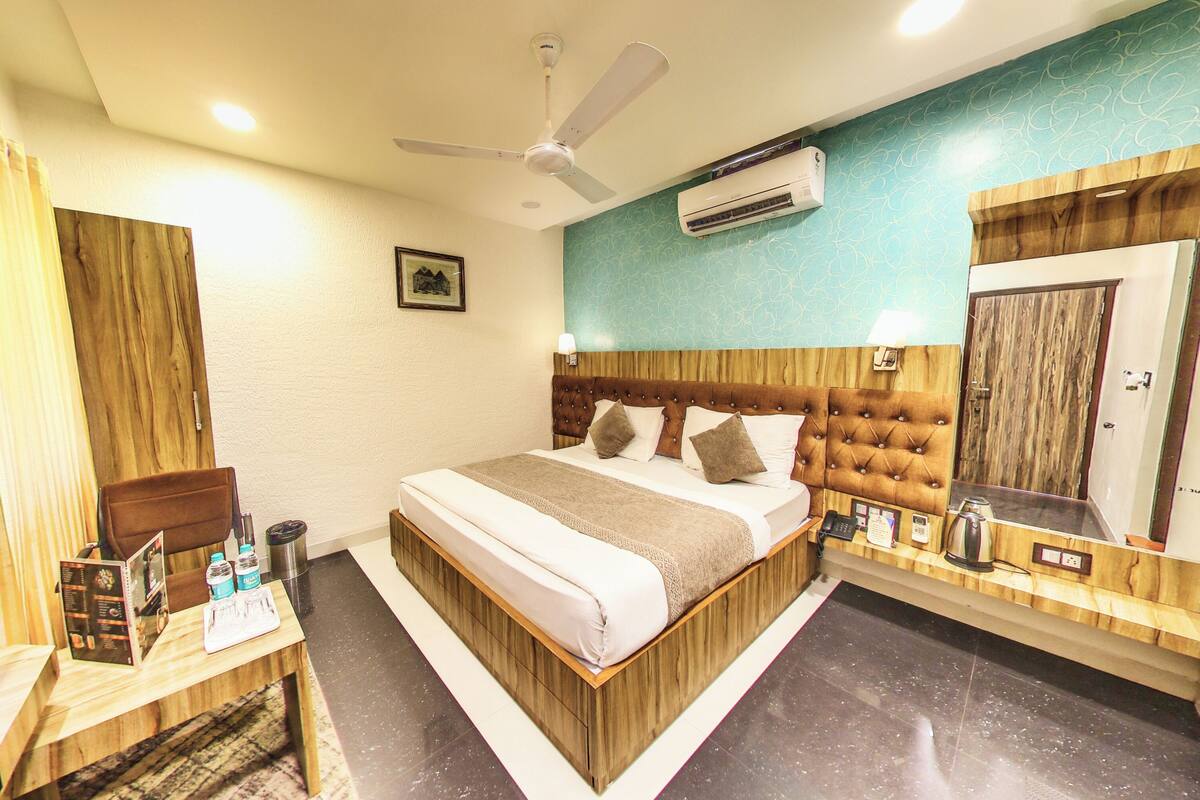 A hotel room with a bed, a desk, a chair, a television, an air conditioner, and a mirror.
