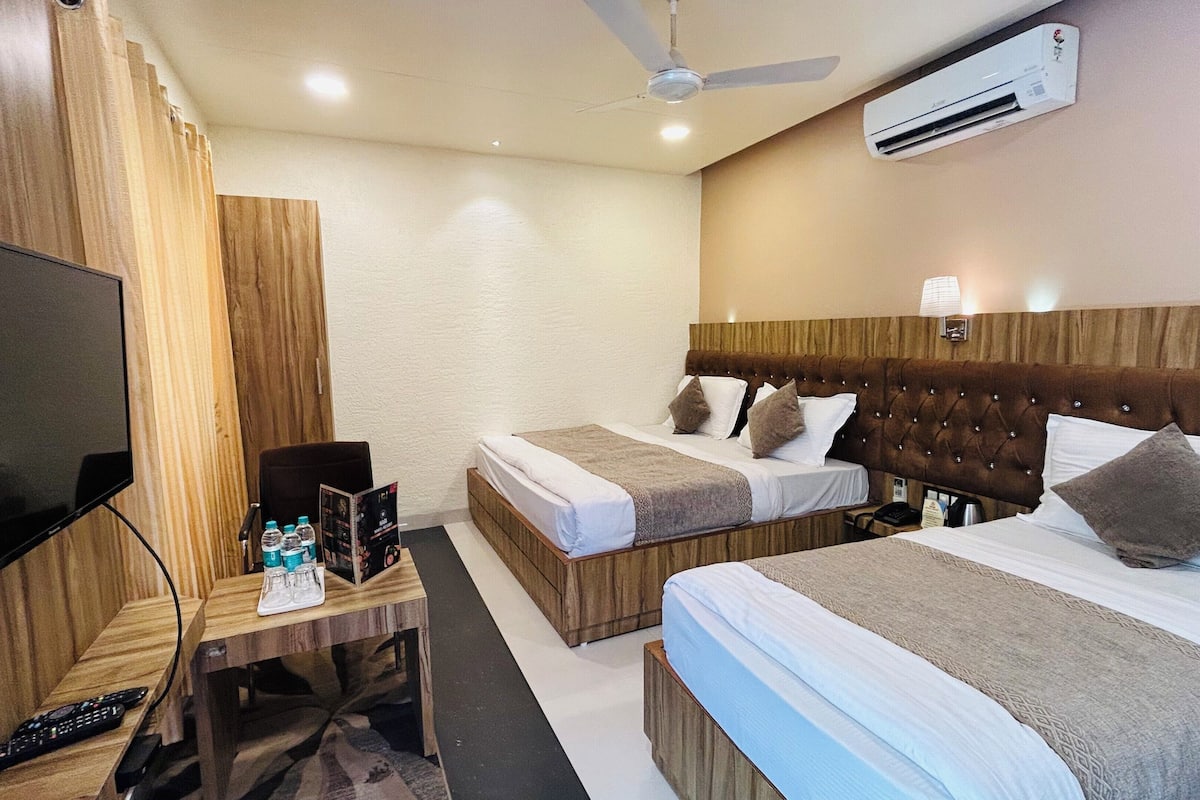 A hotel room with two beds, a TV, a desk with a remote control, and an air conditioner.