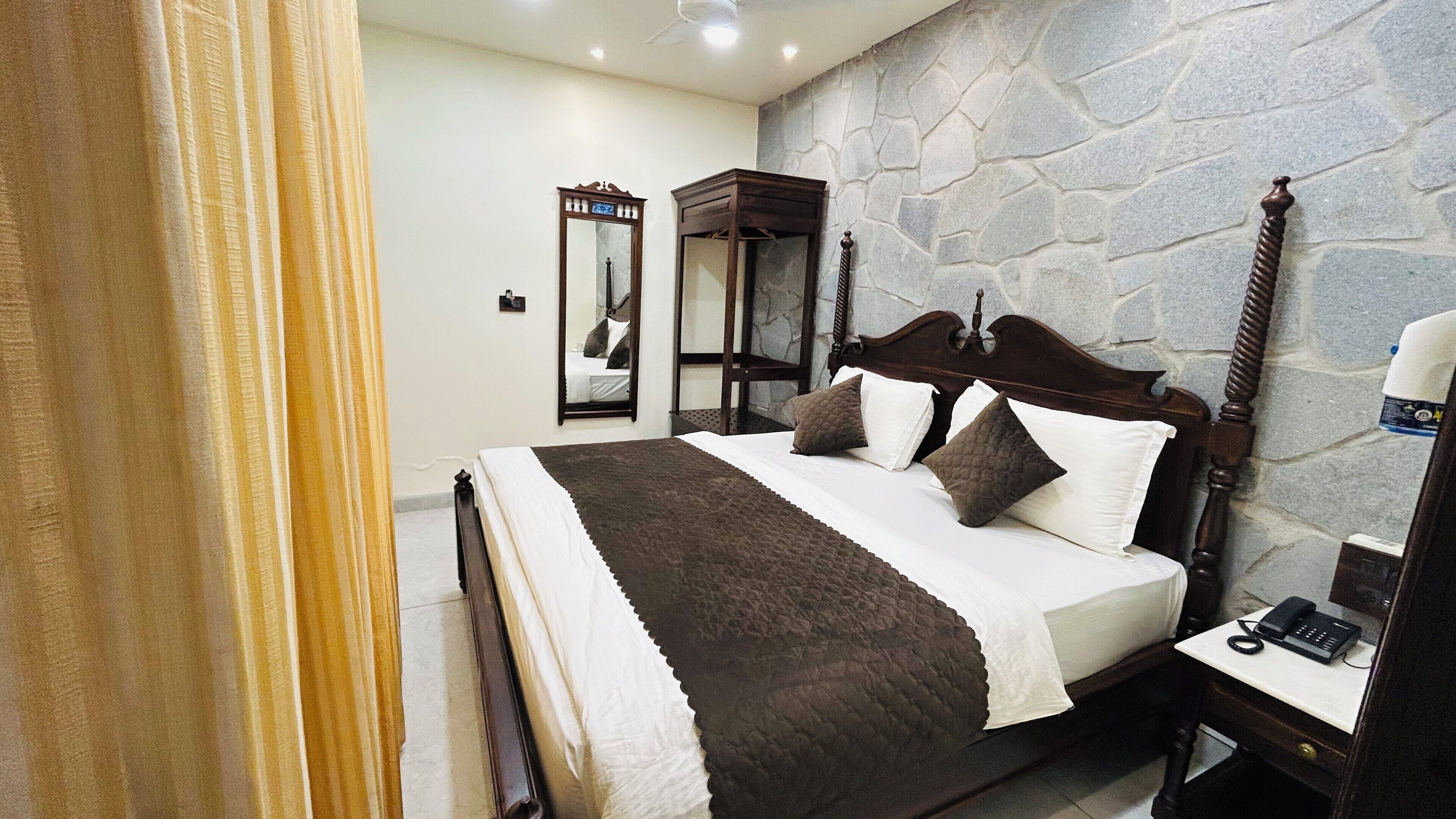 Un dormitorio con una cama grande, cabecera de madera, pared de piedra, mesita de noche con un teléfono y un espejo.
