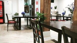 Un'area pranzo con tavoli e sedie di legno, piante in vaso e un estintore sulla parete.