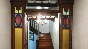 Una scala in legno con un lampadario che conduce a una stanza con un muro azzurro e una finestra colorata.